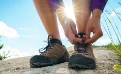 Hiker tying up shoelaces on brown walking shoes on a sunny day
